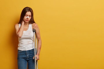 Indoor shot of frustrated woman has accident on motorcycle, touches neck, suffers from pain,...