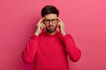 Stressed unshaven man closes eyes, keeps index fingers on temples, feels strong migraine, tries to...