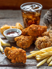 ried chicken, nuggets and french fries, set of junk food with ketchup and one glass of drink on wood table.