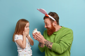 Happy father gives small fluffy rabbit to his daughter, makes present, going to celebrate Easter...