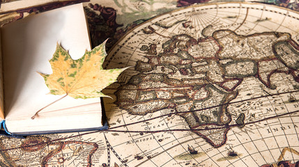 open book and autumn leaf on an old vintage world map, travel and travel theme, tourism