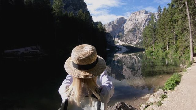 Young caucasian woman in trendy hat making picture on modern mobile phone camera explore scenic landscape of Apls, breathtaking nature of forest and lake in mountains, female blogger photographing