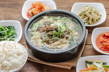 One big set of galbitang, korean style beef soup, serve with many slide dish and rice on wood table with nature light. For food issue.