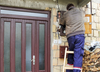 Fototapeta premium Electrician standing on a ladder works in fuse box, next to the front door