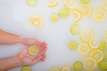 A slice of ripe lime in the hands of a woman. Top view Girl takes a milk bath with lemons. Citrus spa.