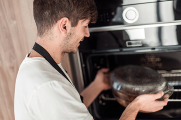 smiling young man warming up dinner in his kitchen