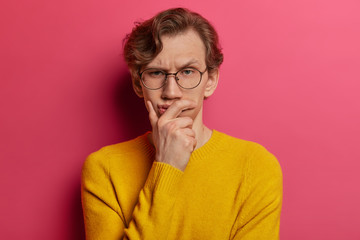 Pensive serious looking man frowns intense and looks directly at camera, holds chin, has...