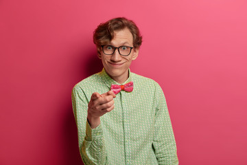 Pleasant looking cheerful European male nerd indicates at camera, has funny look, smiles broadly,...