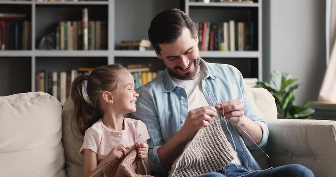 Happy young father having fun teaching little daughter knitting needles