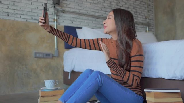 Young Asian woman in bedroom making video call using cell phone, smartphone