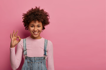 Everything ok. Smiling dark skinned woman has all under control, gives positive reply, recommends good product, assure things are going well, likes something, looks gladfully at camera, stands indoor