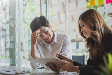 Two young asian business people using tablet working together on business plan in the office.