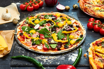 Raw pizza with mozzarella cheese, meat, tomatoes, mushrooms, peppers, herbs on a dark wooden background. Cooking delicious italian pizza.