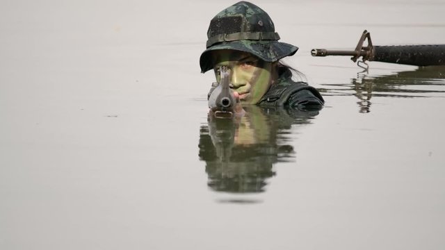 A group of military in war paint black and green face mark wearing green army uniform hiding soak in water their hands holding weapons aiming left and right 