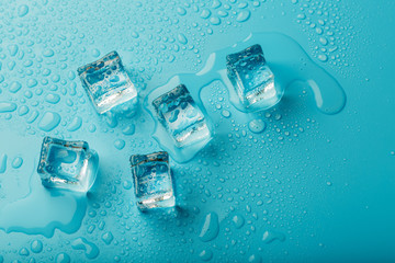 Ice cubes with water drops scattered on a blue background, top view.