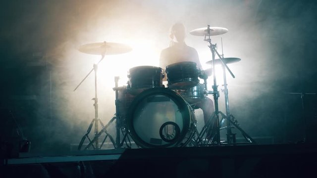 A man is playing the drums in a dark studio with white smoke. Drum set, drum kit in dark, drummer plays a concert.