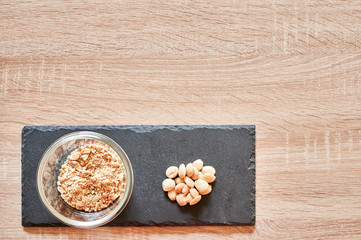 Obraz na płótnie Canvas top view of whole almonds and a bowl of ground almonds on a slate board over a wooden table