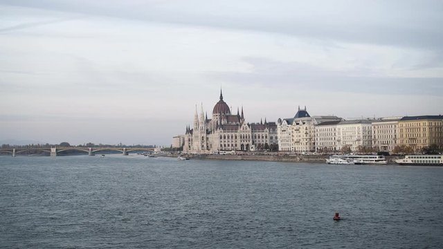 Handheld shot of Hungarian Parliament Building and river Danube, side view shot from the bridge. Handheld shot of Pest, right side of the city under grey blue sky in winter