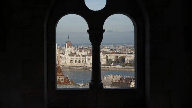 Handheld shot of stepping to Gothic window of the fisherman's Bastion. Overlooking the Parliament in Budapest, under blue sky in winter