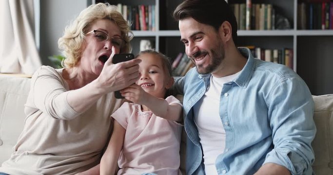Happy multigenerational family using smart phone gadget sit on sofa