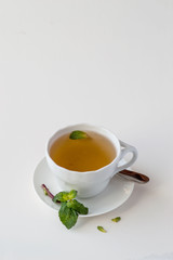 White porcelain cup with fragrant tea and fresh green mint leaves on a light background with copy space. Selective focus.