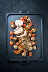 Traditional barbecue rolled lamb roast sliced with tomatoes and mini eggplant as top view on a modern design black tray