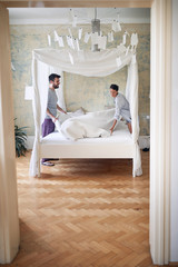young couple smiling, laughing while making bed together in the morning in modern bedroom. couple, togetherness, morning, concept.  © luckybusiness