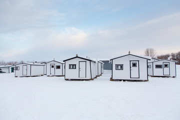 Row of small white huts for ice fishing seen during an early winter morning in Sainte-Anne-de-la-Pérade, Québec, Canada 