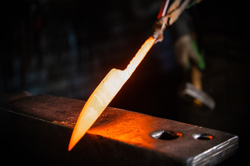 Forging a knife out of the hot metal - holding the knife in forceps - obrazy, fototapety, plakaty
