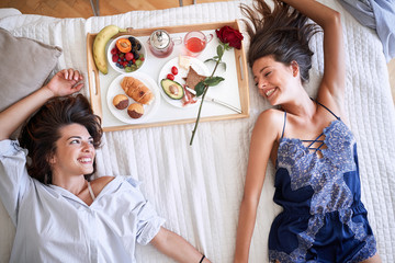 top view of lesbians smiling, holding hands, having breakfast, lying on bed. lesbian, couple,...