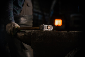 Glowing hammer on the anvil in workshop - a man worker standing on the background