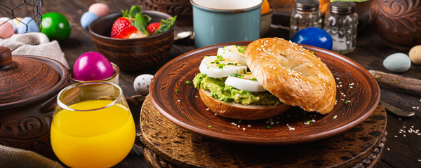 Healthy freshly baked bagel filled with boild eggs, avocado and chives. Breakfast food. Banner.