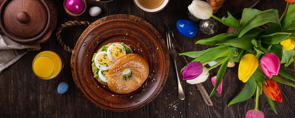 Healthy freshly baked bagel filled with boild eggs, avocado and chives. Breakfast food, top view, banner