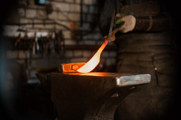Forging a knife out of the hot metal - holding the knife between the forceps