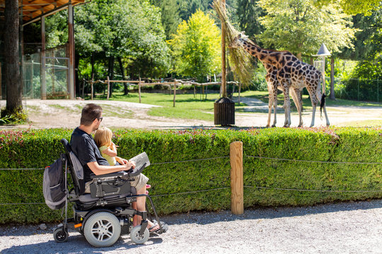 Disabled Father in Wheelchair enjoying Nature with Daughter Girl in Outside zoo park on a sunny day.