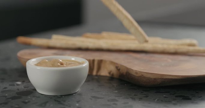 Slow motion man hand dip grissini in cashew paste in white bowl on terrazzo countertop