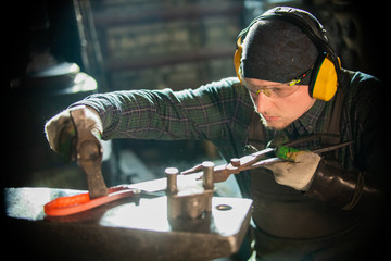 A man blacksmith in protective glasses making a unique item - bending the metal