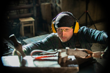 A man blacksmith in protective glasses making a unique handle