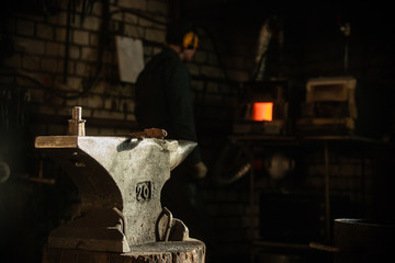 A hammer on the anvil in natural sun lighting in workshop - blacksmith standing on the background