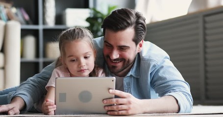 Dad and small daughter using digital tablet lying on floor - Powered by Adobe