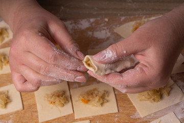 A woman sculpts dumplings and ravioli from squares of dough and cabbage. Plywood cutting board, wooden flour sieve and wooden rolling pin - tools for making dough.