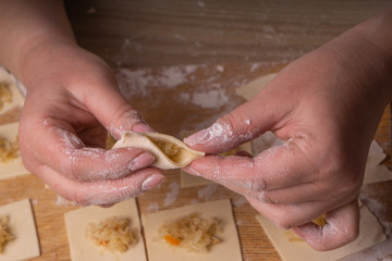 A woman sculpts dumplings and ravioli from squares of dough and cabbage. Plywood cutting board, wooden flour sieve and wooden rolling pin - tools for making dough. - Powered by Adobe