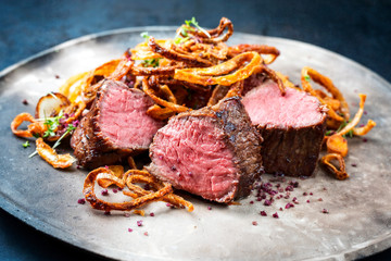 Traditionelles dry aged Rinderfilet natur aufgeschnitten mit Röstzwiebel und Bratkartoffel angeboten als closeup auf einem Modern Design Teller