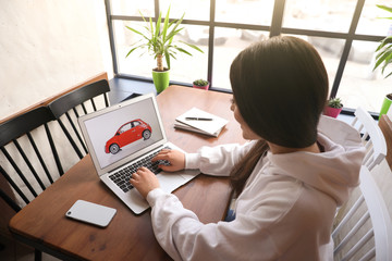 Woman using laptop to buy car at wooden table indoors