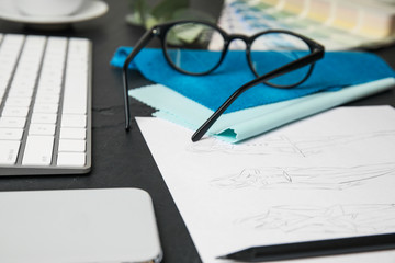 Sketches of clothes, smartphone and keyboard on black stone table, closeup. Designer's workplace