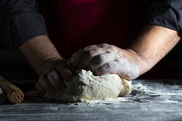 Man's hands knead the dough. Close-up. Dark background