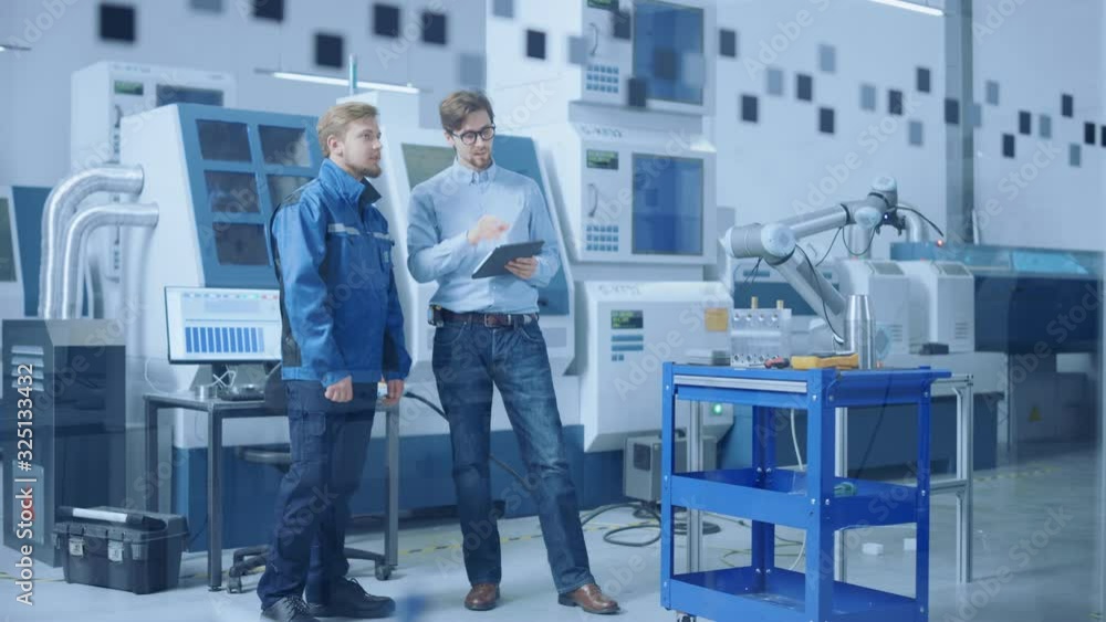 Leinwandbilder Modern Factory: Project Manager and Engineer Standing, Talking, Using Tablet Computer for Programming and Manipulating Robot Arm for Assembly Line. Industry 4.0 Facility with High Tech CNC Machinery