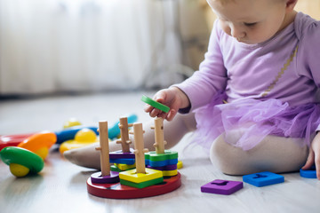 girl plays toys in living room. Montessori wooden toy folded pyramid. Circle, quadra, triangle,...