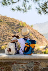 Healthy and adventurous lifestyle concept with kid hugging dog on stone bench looking at mountains (view from behind)