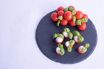 basil, round mozzarella and tomatoes on a black tile